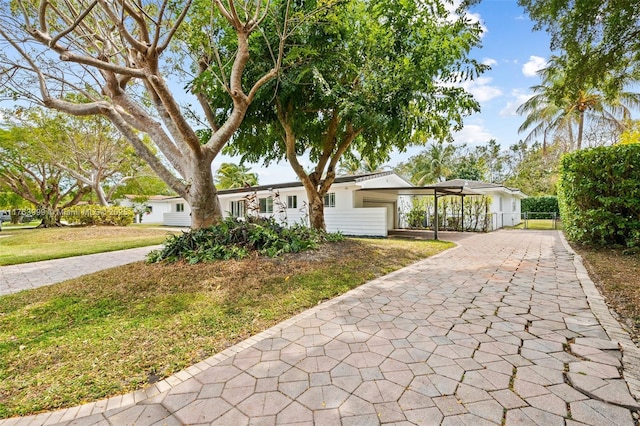 ranch-style home featuring a front lawn, decorative driveway, and a carport