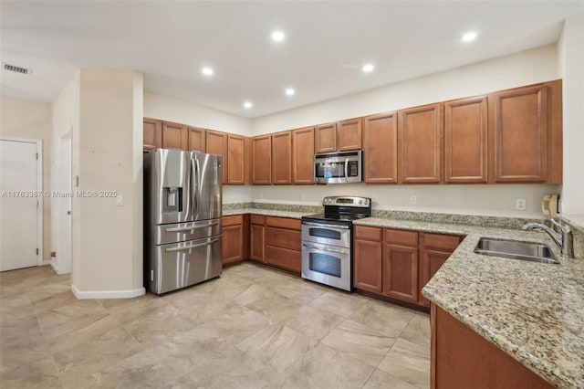 kitchen with visible vents, light stone counters, brown cabinets, stainless steel appliances, and a sink