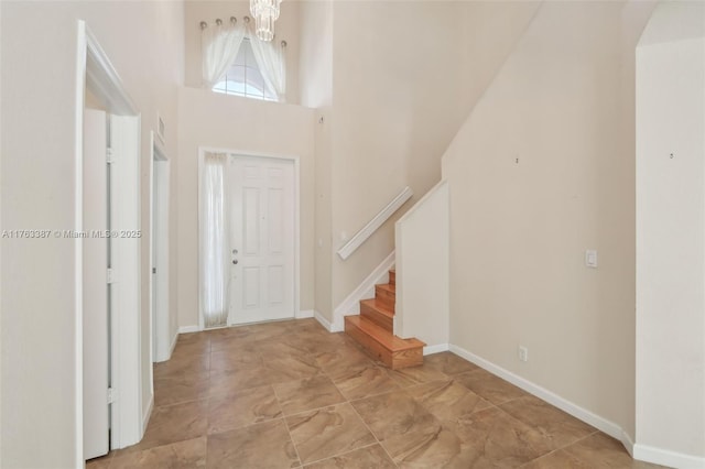 foyer featuring a chandelier, baseboards, stairs, and a towering ceiling