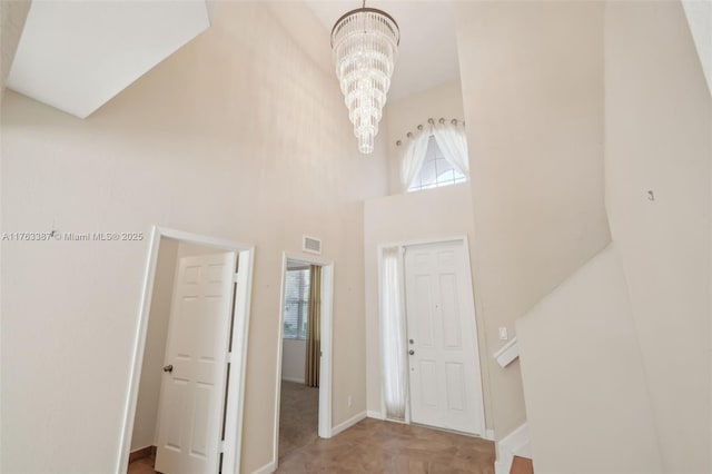 entryway with visible vents, baseboards, a notable chandelier, and a high ceiling