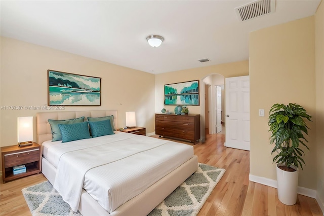 bedroom with visible vents, arched walkways, baseboards, and light wood-style flooring