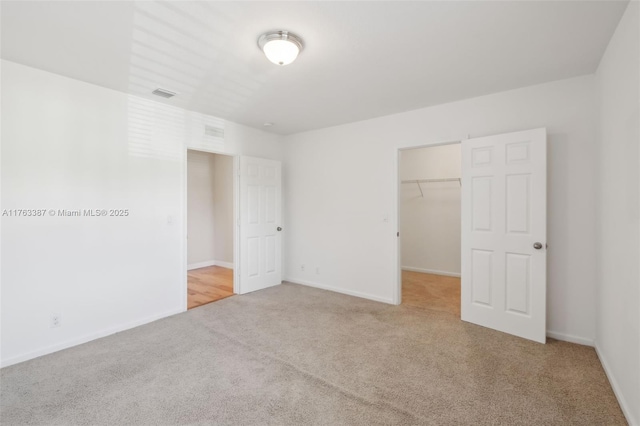 unfurnished bedroom with visible vents, a walk in closet, a closet, carpet flooring, and baseboards