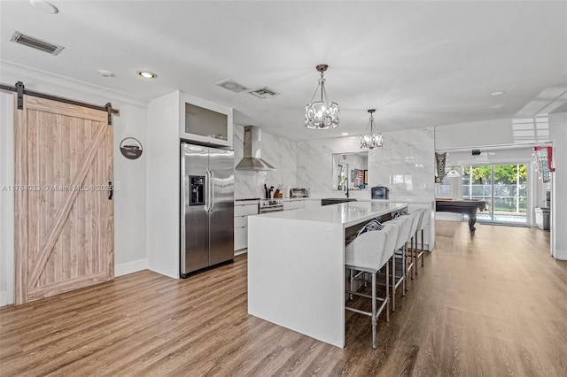 kitchen featuring visible vents, wood finished floors, appliances with stainless steel finishes, wall chimney exhaust hood, and light countertops