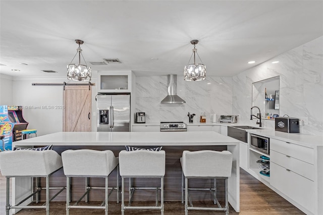 kitchen featuring an inviting chandelier, wall chimney exhaust hood, appliances with stainless steel finishes, and a sink