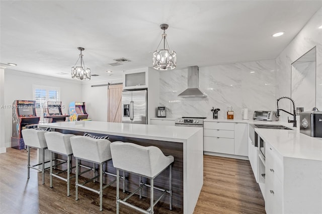 kitchen with an inviting chandelier, appliances with stainless steel finishes, wall chimney range hood, modern cabinets, and tasteful backsplash