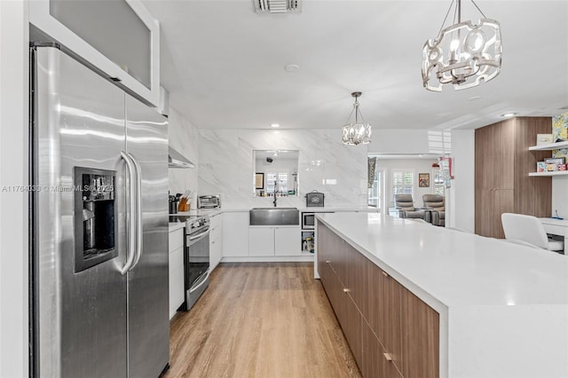 kitchen with modern cabinets, a sink, appliances with stainless steel finishes, an inviting chandelier, and light wood finished floors