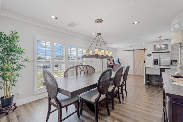 dining space featuring light wood-type flooring, a barn door, baseboards, and ornamental molding