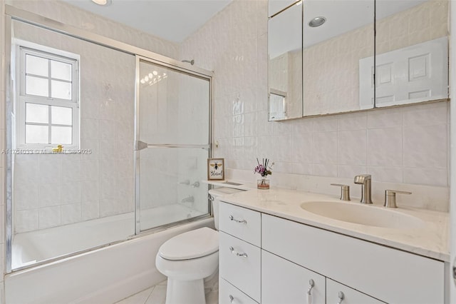 bathroom featuring backsplash, toilet, vanity, shower / bath combination with glass door, and tile walls