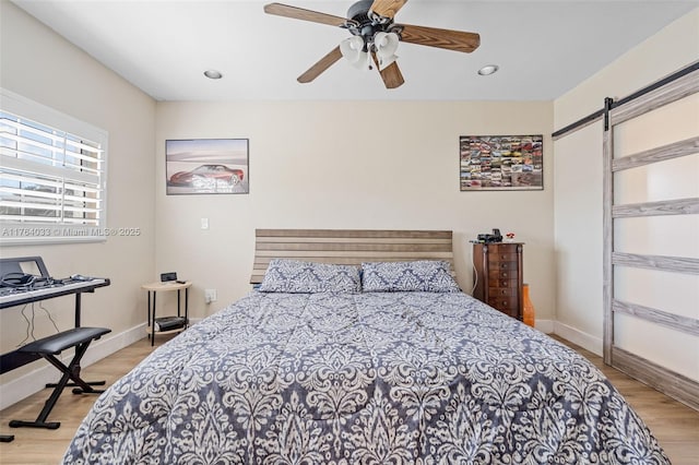 bedroom with a barn door, light wood-style flooring, baseboards, and ceiling fan