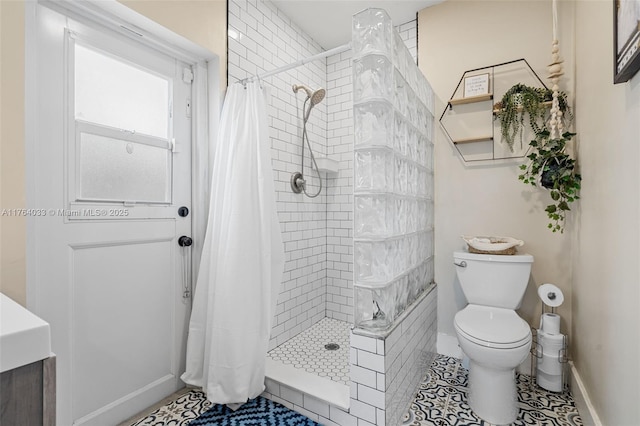 full bath featuring tile patterned flooring, toilet, baseboards, and a tile shower