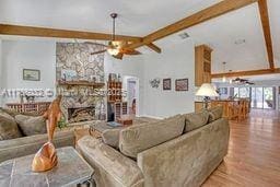 living room featuring a fireplace, wood finished floors, beamed ceiling, and a ceiling fan