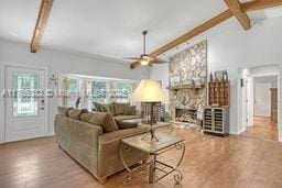 living room with a fireplace, vaulted ceiling with beams, wood finished floors, and ceiling fan