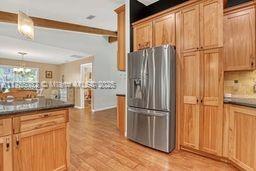 kitchen featuring beam ceiling, light wood-style flooring, stainless steel refrigerator with ice dispenser, dark countertops, and a chandelier