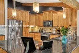 kitchen with dark countertops, hanging light fixtures, beamed ceiling, and appliances with stainless steel finishes