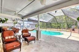 outdoor pool featuring glass enclosure, a patio, and ceiling fan