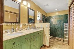 full bathroom featuring double vanity, wood finished floors, a walk in shower, and a sink