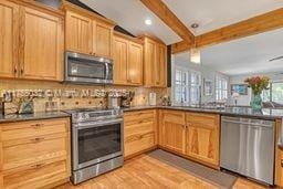 kitchen with light brown cabinets, a peninsula, beam ceiling, light wood-style floors, and appliances with stainless steel finishes