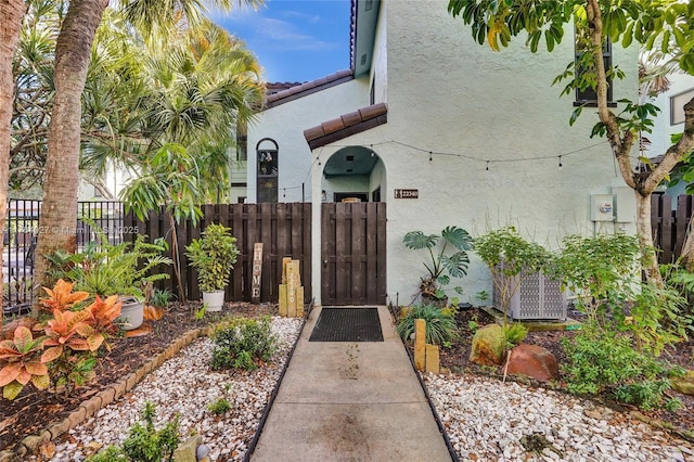 property entrance with stucco siding, a gate, central AC, fence, and a tiled roof