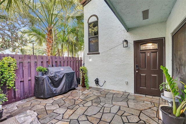 property entrance with stucco siding, a patio, and fence