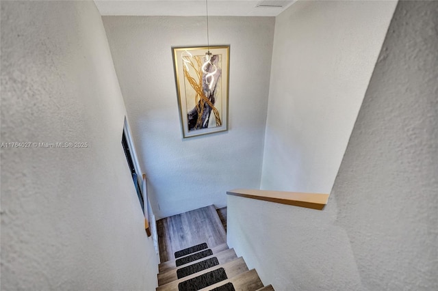 stairway featuring wood finished floors and a textured wall