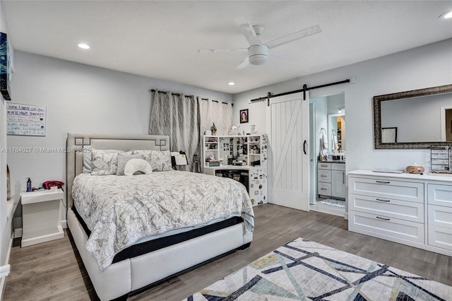 bedroom with a ceiling fan, ensuite bathroom, wood finished floors, recessed lighting, and a barn door