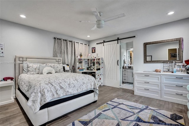 bedroom with wood finished floors, recessed lighting, a barn door, connected bathroom, and ceiling fan