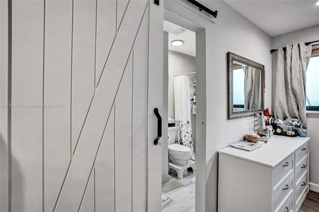 full bath with a shower with curtain, toilet, wood finished floors, vanity, and a textured wall