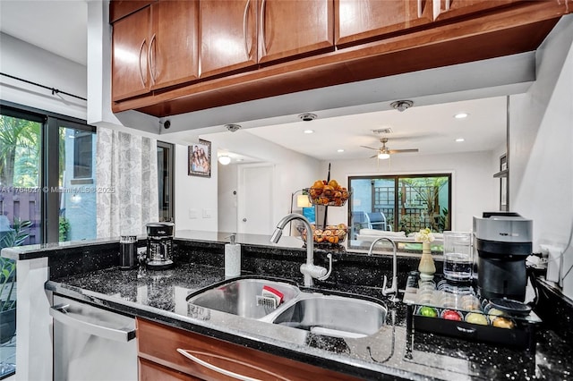 kitchen featuring brown cabinetry, stainless steel dishwasher, dark stone counters, and a sink