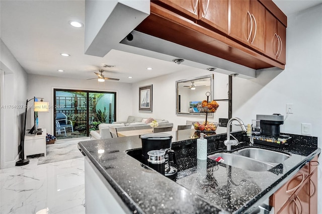 kitchen with brown cabinetry, dark stone countertops, a ceiling fan, and a sink