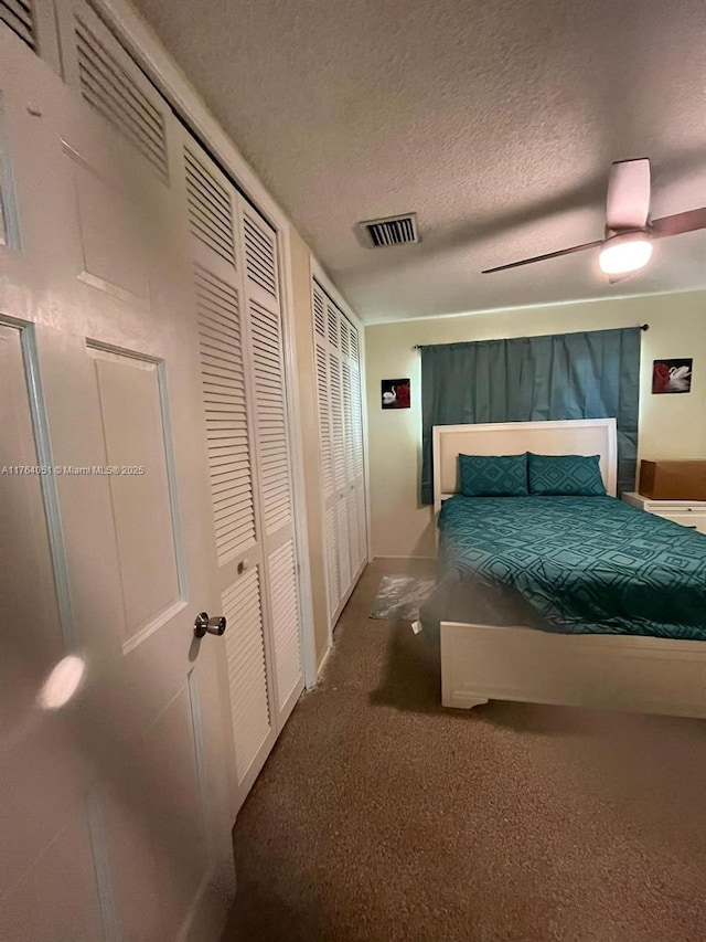 bedroom with visible vents, a textured ceiling, carpet floors, baseboards, and ceiling fan