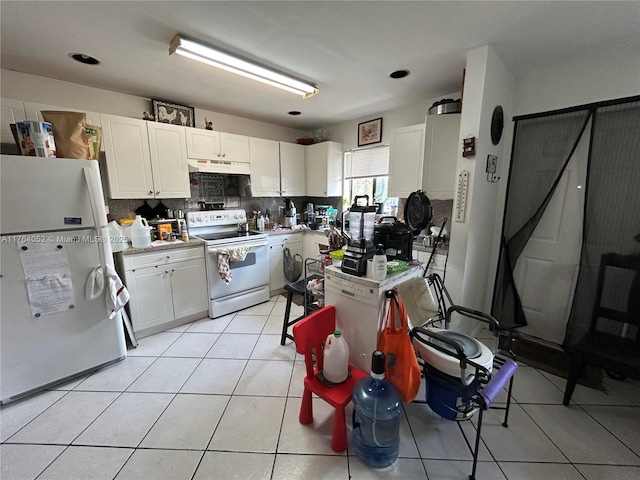 kitchen featuring backsplash, under cabinet range hood, light tile patterned flooring, white appliances, and white cabinetry