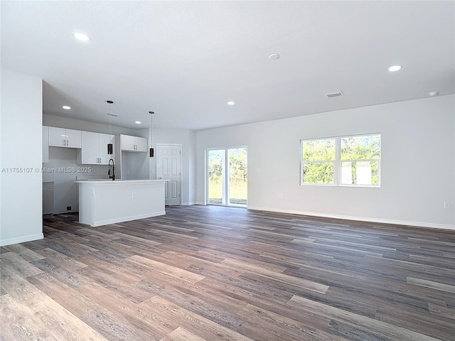 unfurnished living room featuring visible vents, a sink, wood finished floors, recessed lighting, and baseboards