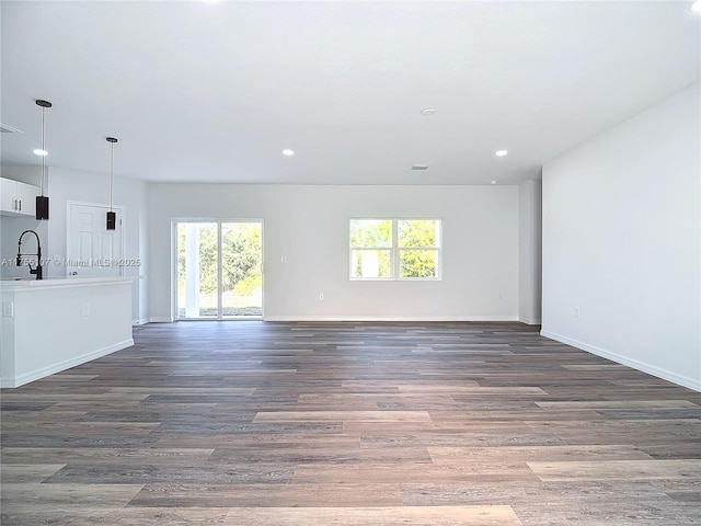 unfurnished living room featuring wood finished floors, baseboards, and a sink