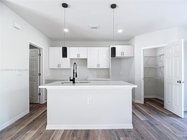 kitchen with wood finished floors, visible vents, an island with sink, a sink, and white cabinetry