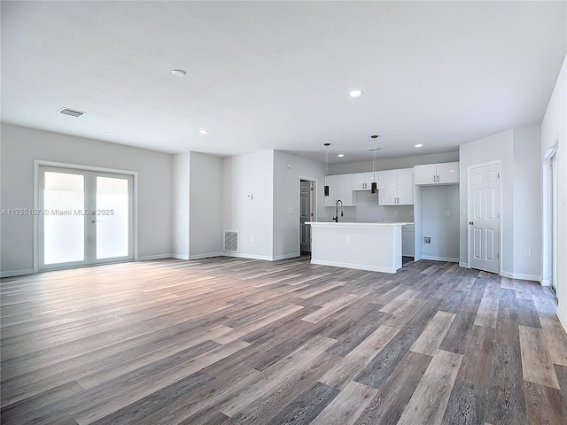 unfurnished living room featuring wood finished floors, baseboards, visible vents, recessed lighting, and a sink