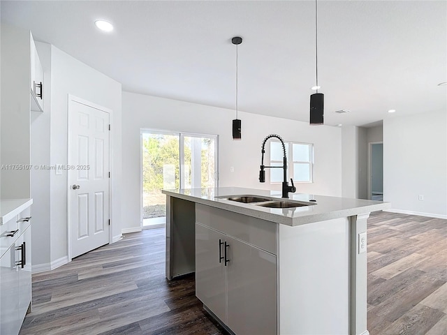 kitchen with wood finished floors, baseboards, a kitchen island with sink, a sink, and light countertops