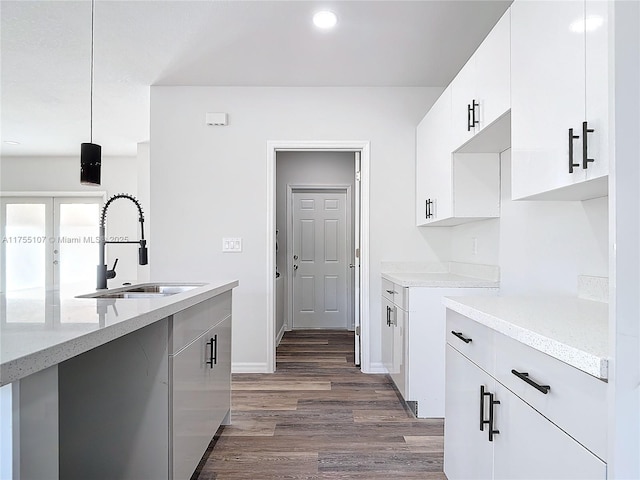 kitchen with dark wood-style floors, baseboards, light stone countertops, a sink, and white cabinets