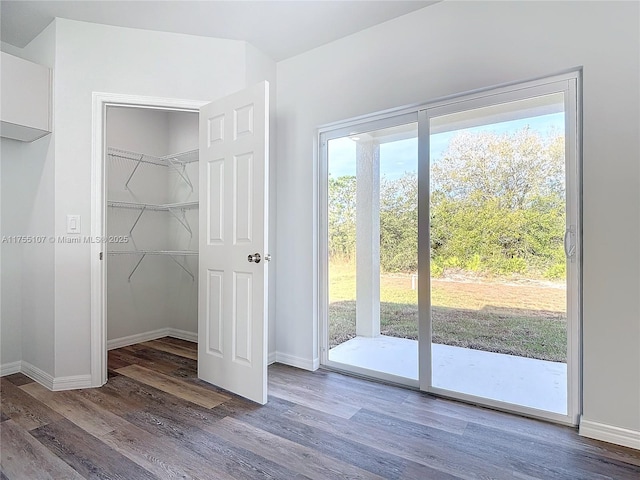 unfurnished bedroom featuring access to exterior, multiple windows, baseboards, and wood finished floors