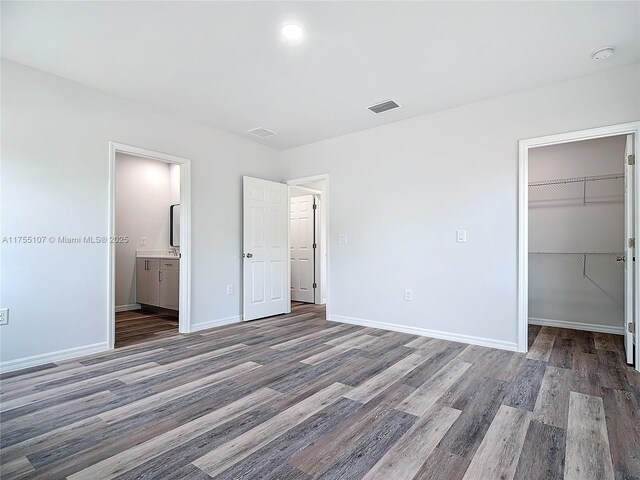 unfurnished bedroom with visible vents, a walk in closet, baseboards, and wood finished floors