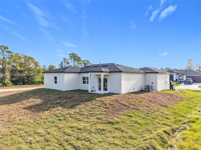 back of house featuring central AC unit, stucco siding, french doors, and a lawn