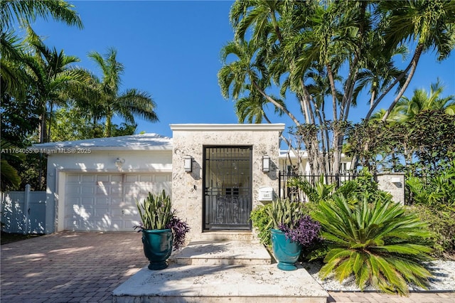 view of exterior entry featuring stucco siding, an attached garage, driveway, and fence