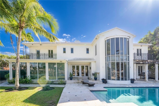 back of property featuring a balcony, an outdoor pool, stucco siding, french doors, and a patio area