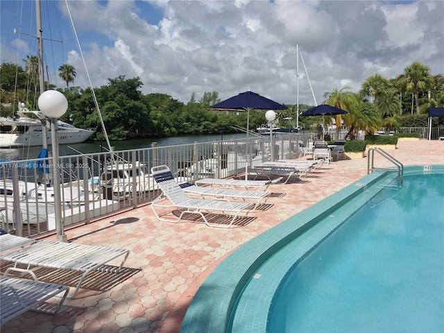 community pool featuring a patio area, a water view, and fence