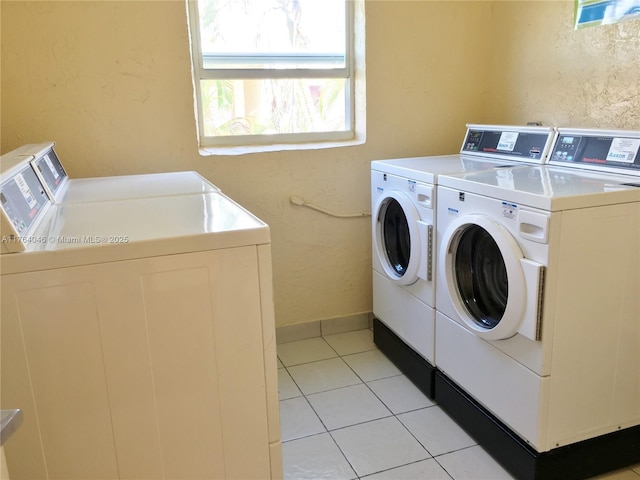 common laundry area featuring light tile patterned floors, baseboards, washing machine and dryer, and a textured wall