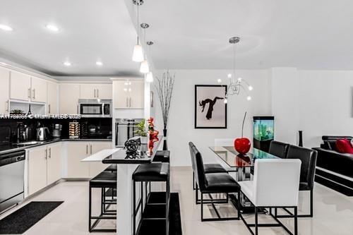 kitchen with white cabinets, pendant lighting, dishwasher, stainless steel microwave, and a kitchen bar