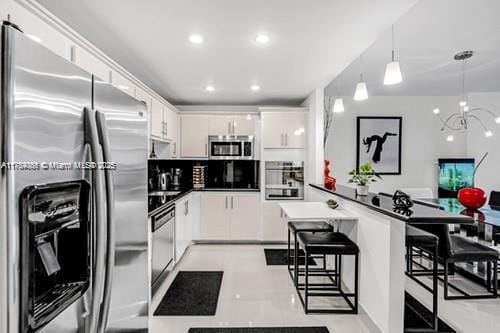 kitchen with a breakfast bar, a peninsula, stainless steel appliances, white cabinets, and a notable chandelier