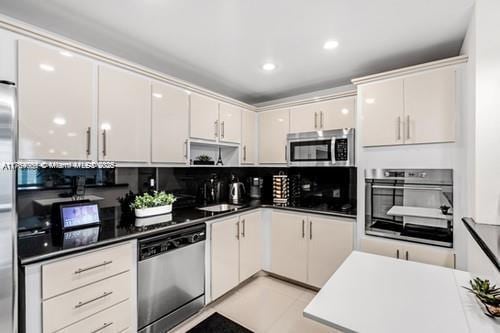 kitchen with recessed lighting, decorative backsplash, white cabinets, appliances with stainless steel finishes, and dark countertops