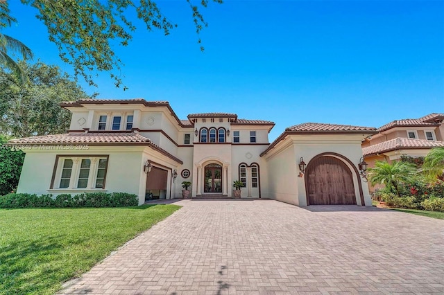 mediterranean / spanish home featuring a front lawn, a tiled roof, stucco siding, decorative driveway, and an attached garage