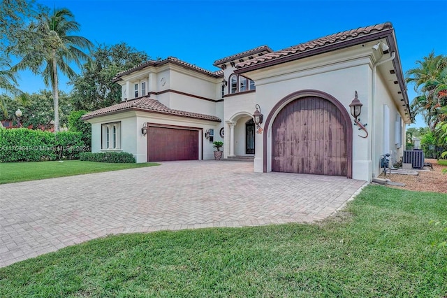 mediterranean / spanish house with central air condition unit, stucco siding, a front lawn, decorative driveway, and a tiled roof