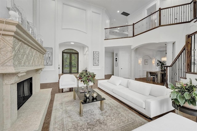 living area featuring arched walkways, a fireplace, baseboards, stairs, and ornate columns